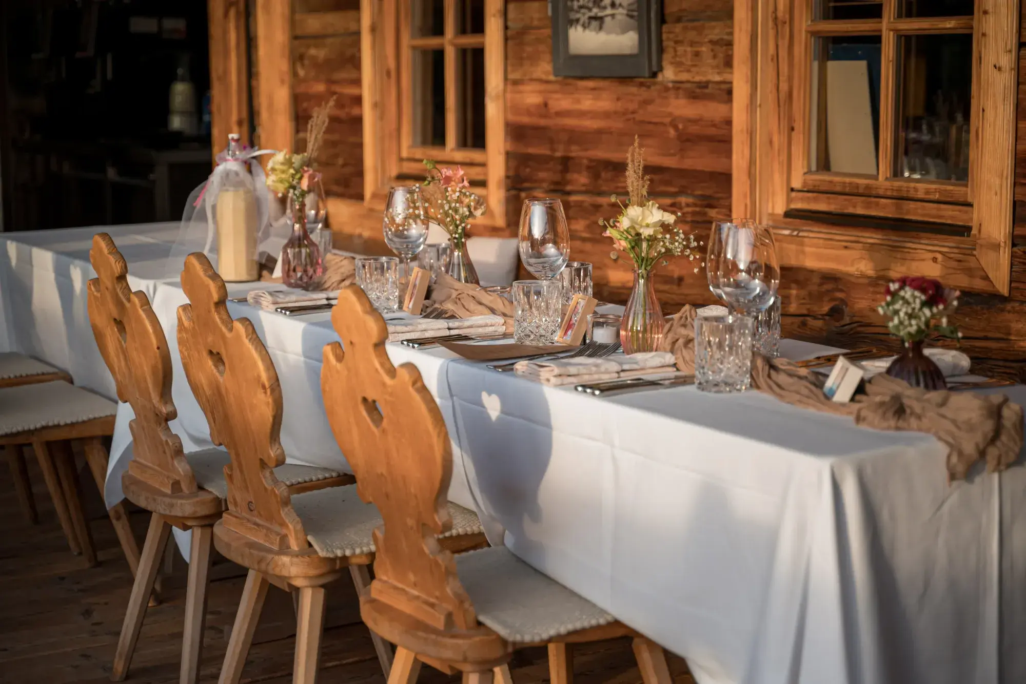 Familienfeier an festlich gedeckter Tafel mit geschnitzten Tiroler Holzstühlen vor der Holzfassade der Stöttlalm