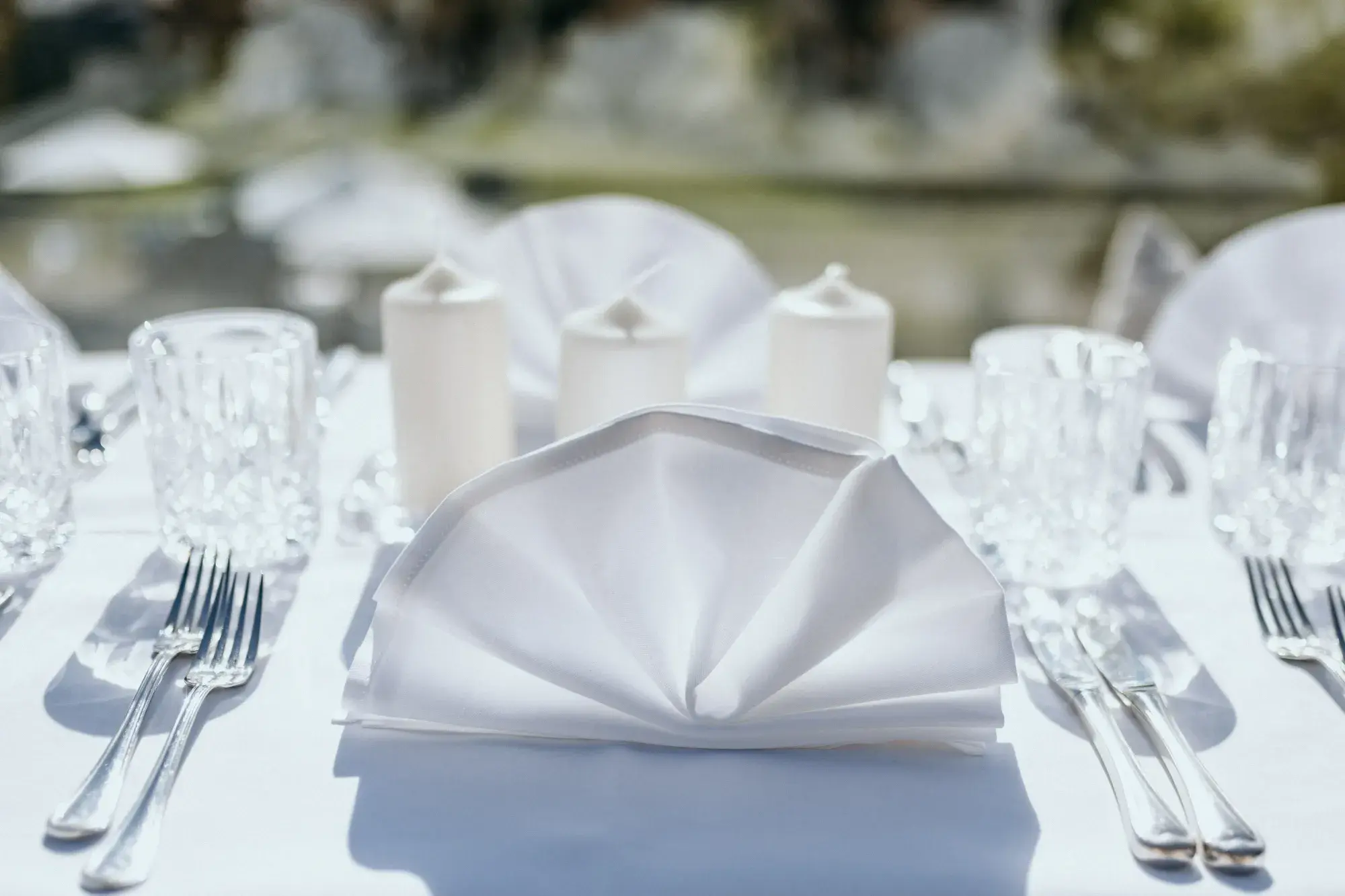 Kunstvoll gefächerte weiße Serviette mit Kerzen und Kristallgläsern auf der Festtafel im Freien an der Stöttlalm