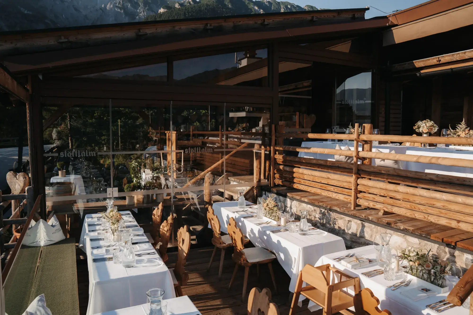 Lange gedeckte Festtafeln mit Tiroler Holzstühlen auf der Terrasse der Stöttlalm im Abendlicht vor der Mieminger Kette