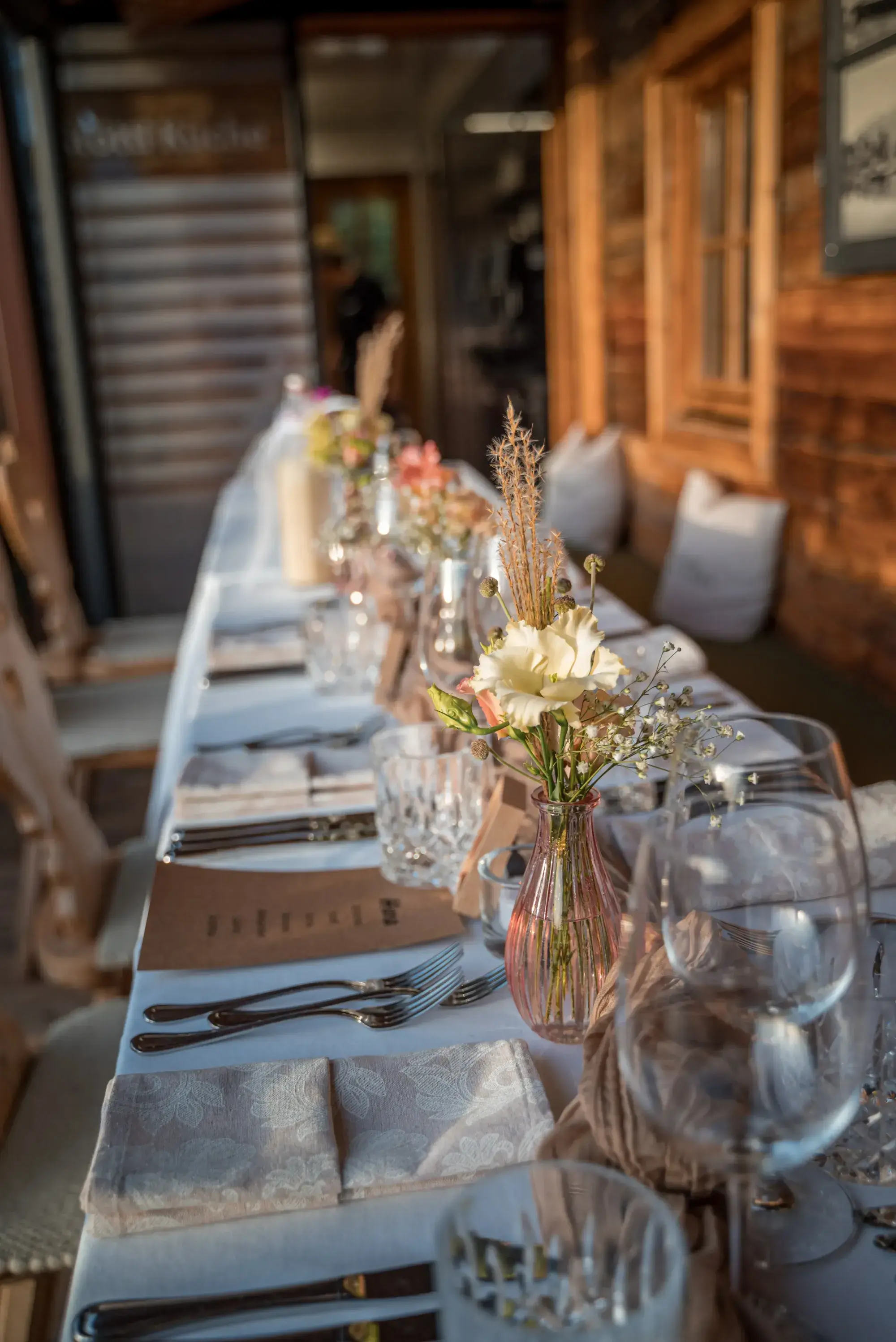 Lange weiß gedeckte Festtafel mit Trockenblumen und Kristallgläsern auf der Terrasse der Stöttlalm für Firmenfeiern