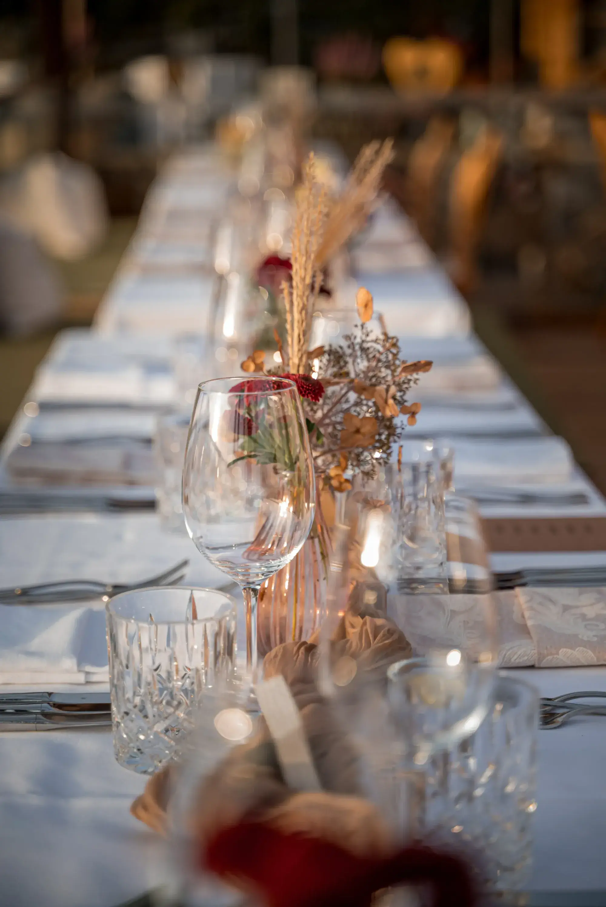 Lange weiß gedeckte Festtafel mit Trockenblumen und Kerzenlicht in abendlicher Stimmung auf der Stöttlalm