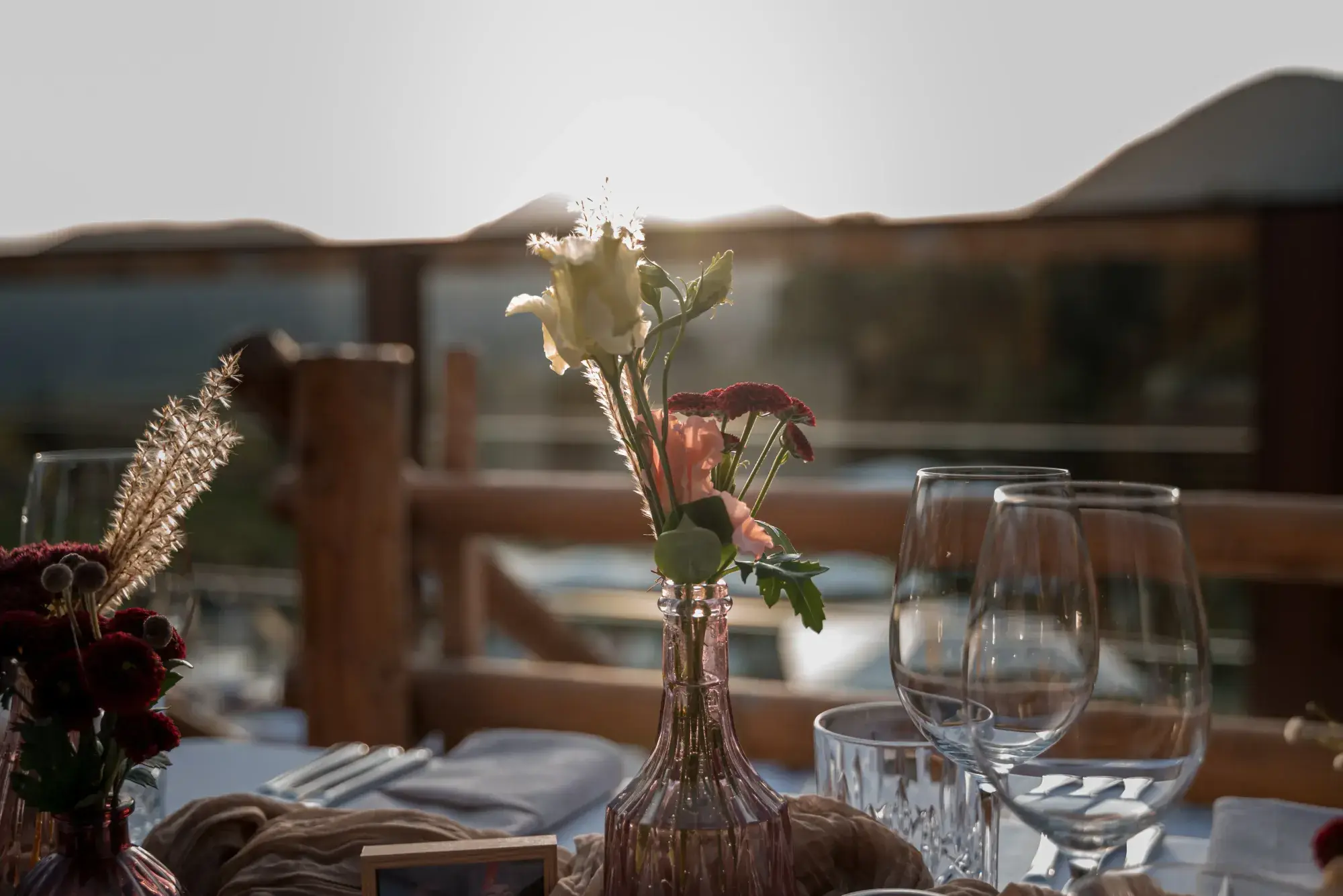 Zarte Blumendeko in rosafarbener Vase auf der Terrassentafel der Stöttlalm im Gegenlicht des Sonnenuntergangs