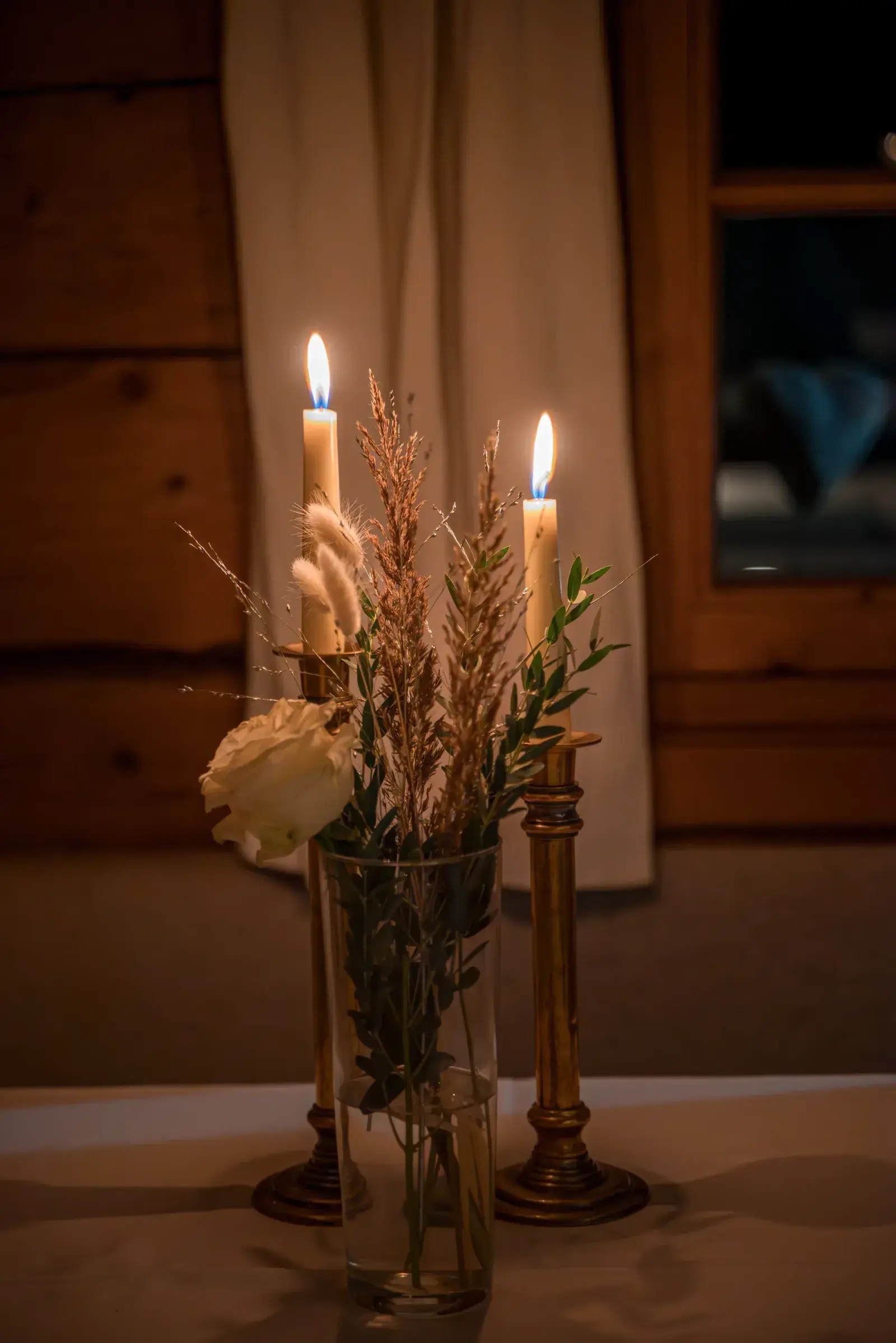 Stimmungsvolle Tischdeko bei Kerzenschein mit weißer Rose und Trockenblumen in der gemütlichen Stube der Stöttlalm