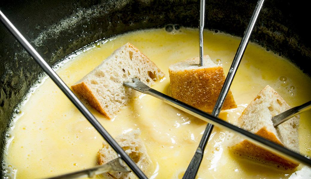 Brotwürfel werden mit Fonduegabeln in geschmolzenes Käsefondue getaucht, Tiroler Spezialität der Stöttlalm