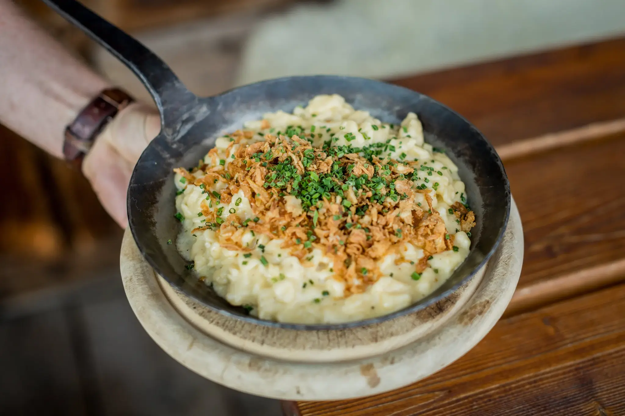 Dampfende Tiroler Käsespätzle mit Röstzwiebeln und Schnittlauch in der Pfanne, Spezialität der Stöttlalm